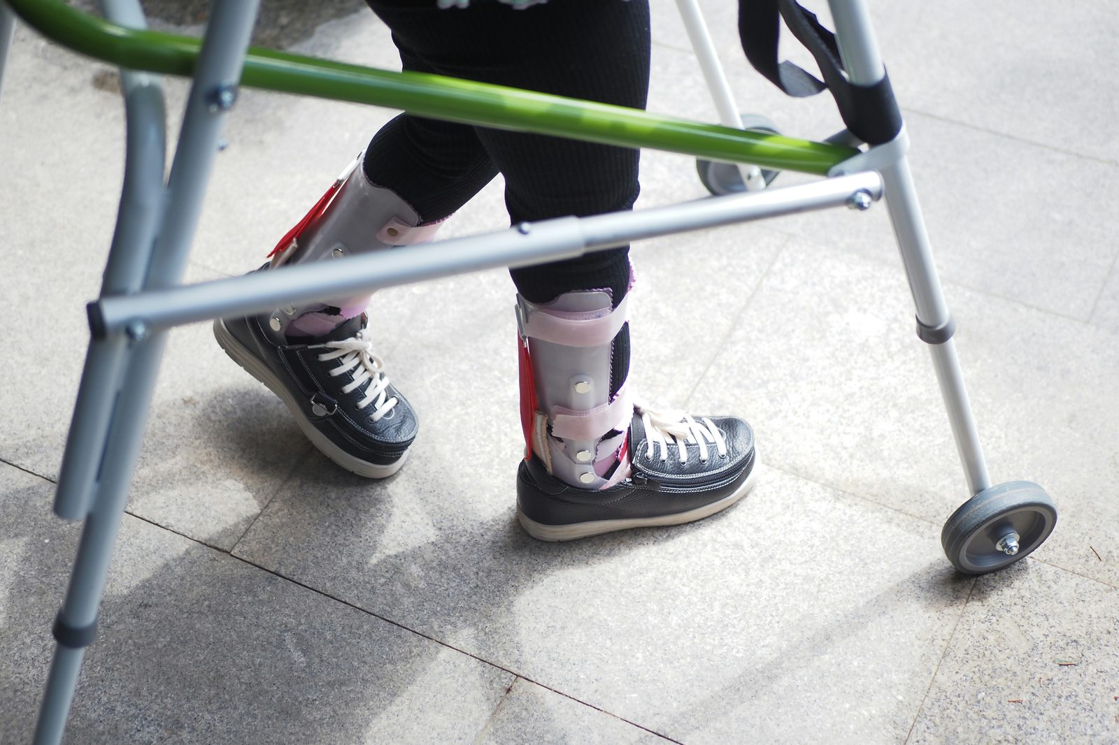 Child with ankle-foot orthoses using a walking frame, photographed waist-down