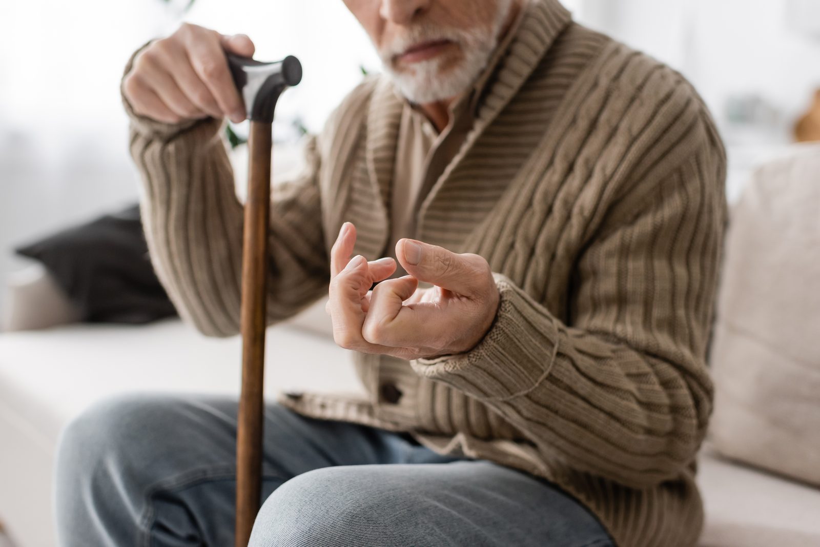 Older man with a walking cane, hand showing tremor, in a calm home setting